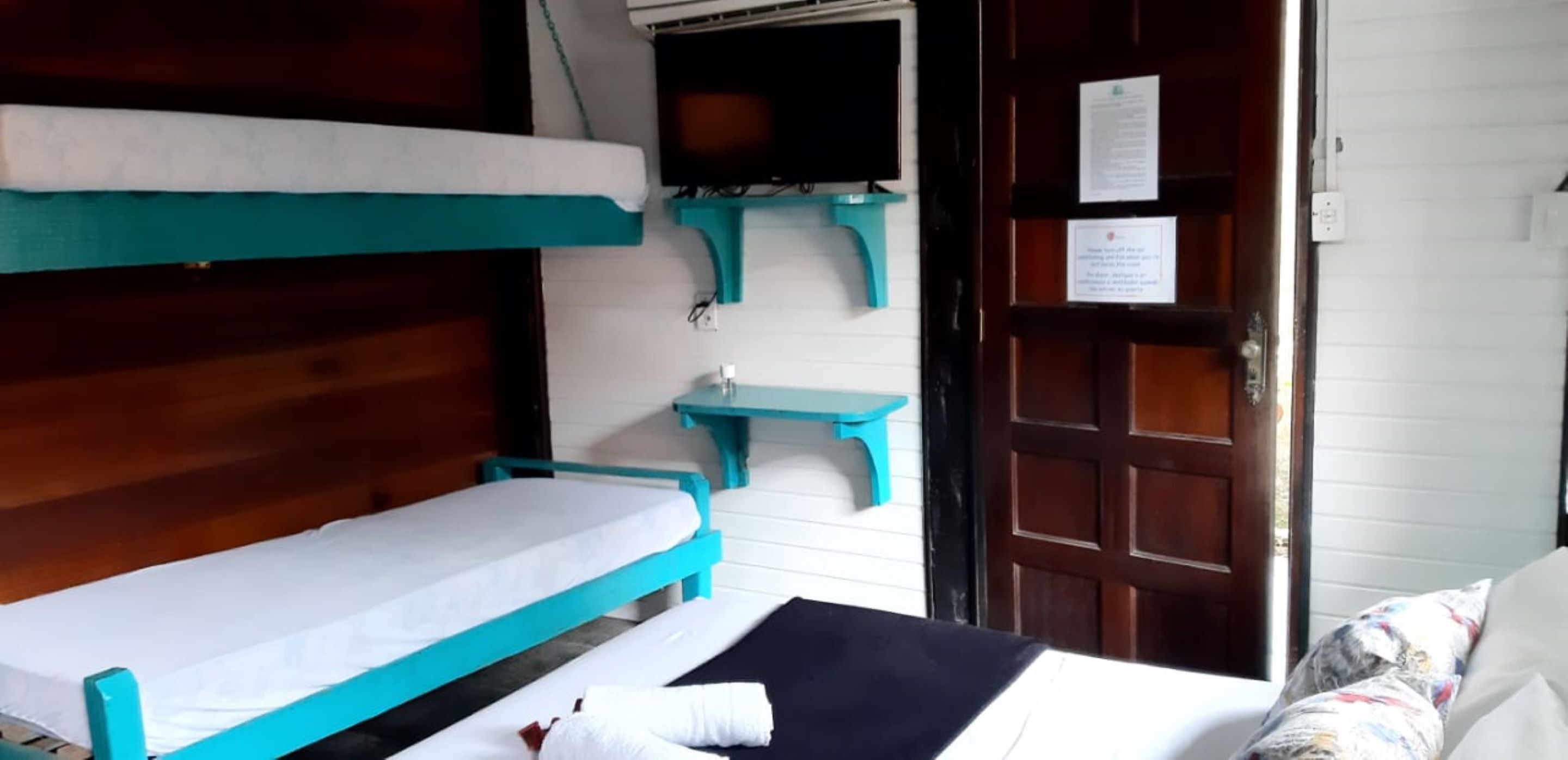 Een kamer met een stapelbed, een enkel bed, een kleine tafel en een deur met een bordje.