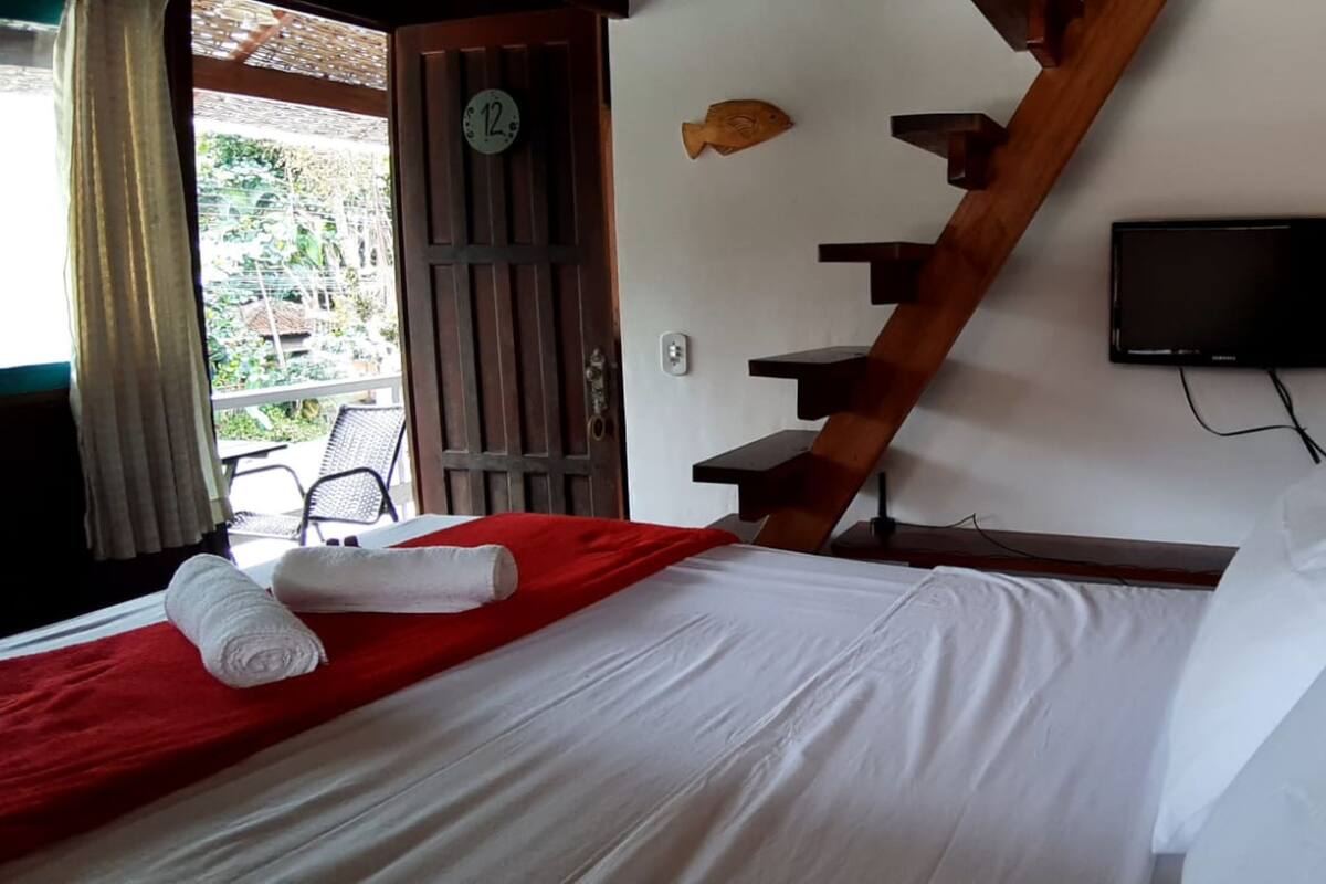 A hotel room with a bed, a TV mounted on the wall, a wooden staircase, and a view of the outside.
