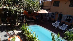 A swimming pool surrounded by outdoor furniture, including chairs and a table, with a patio area and a building in the background. - Hostel Sereia do Mar (Paraty)