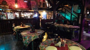A restaurant interior with round tables covered in floral tablecloths, chairs, and a bar area in the background. - Hostel Sereia do Mar (Paraty)