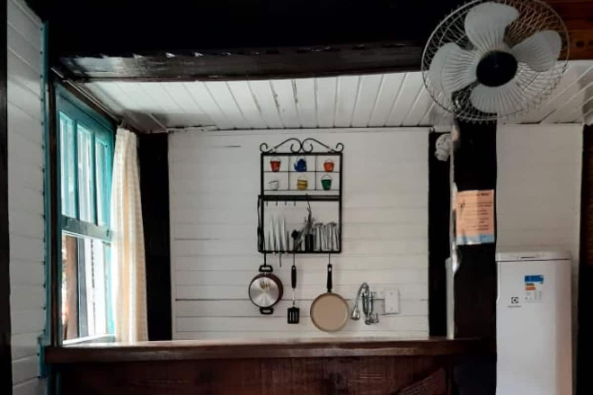 A room with a wooden bed, a white wall with kitchen utensils, a fan, and a window with curtains.