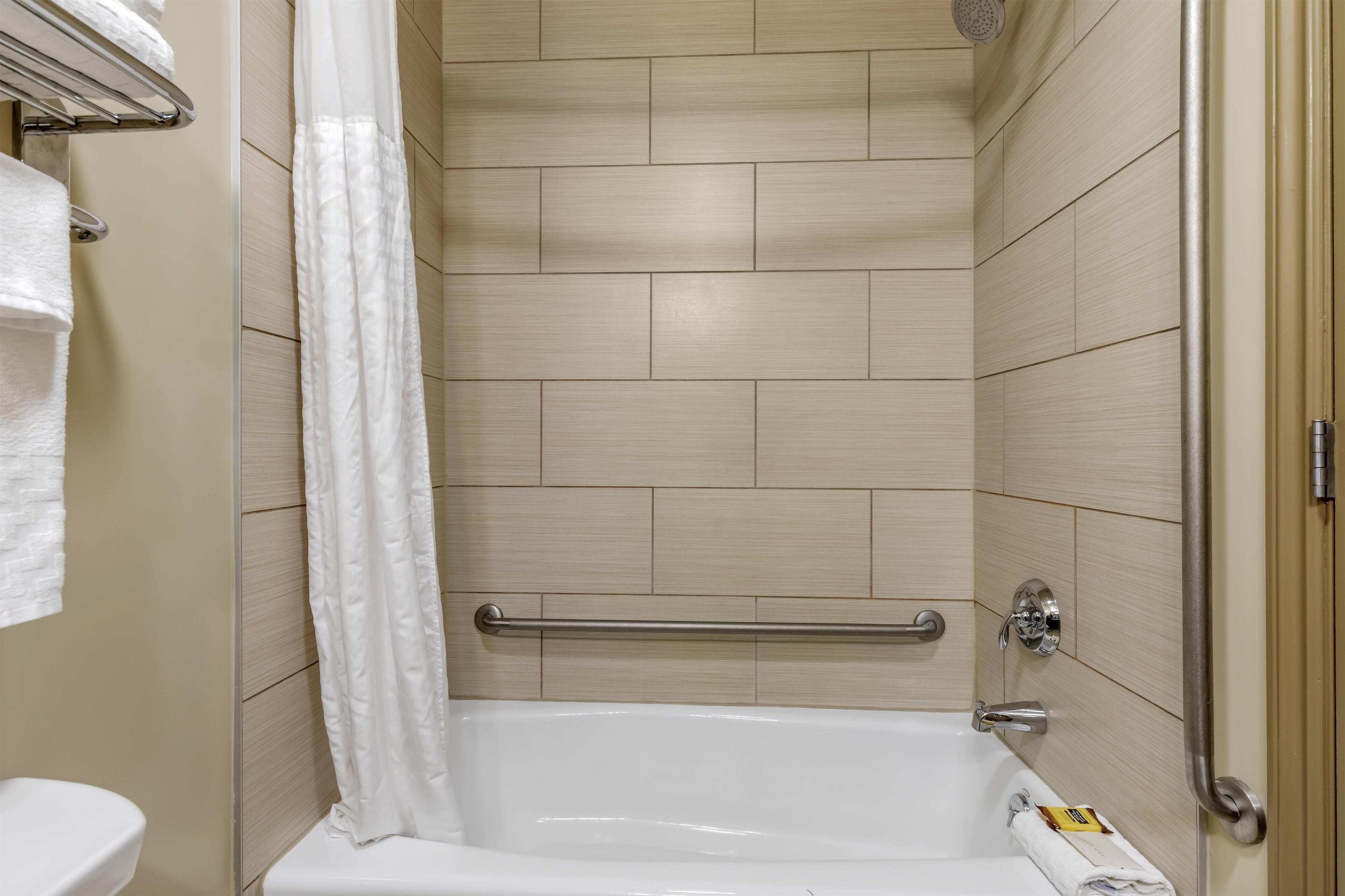A bathroom with a bathtub, a shower curtain, and a handrail.