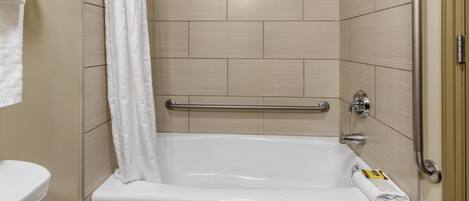 A bathroom with a bathtub, a shower curtain, and a handrail.