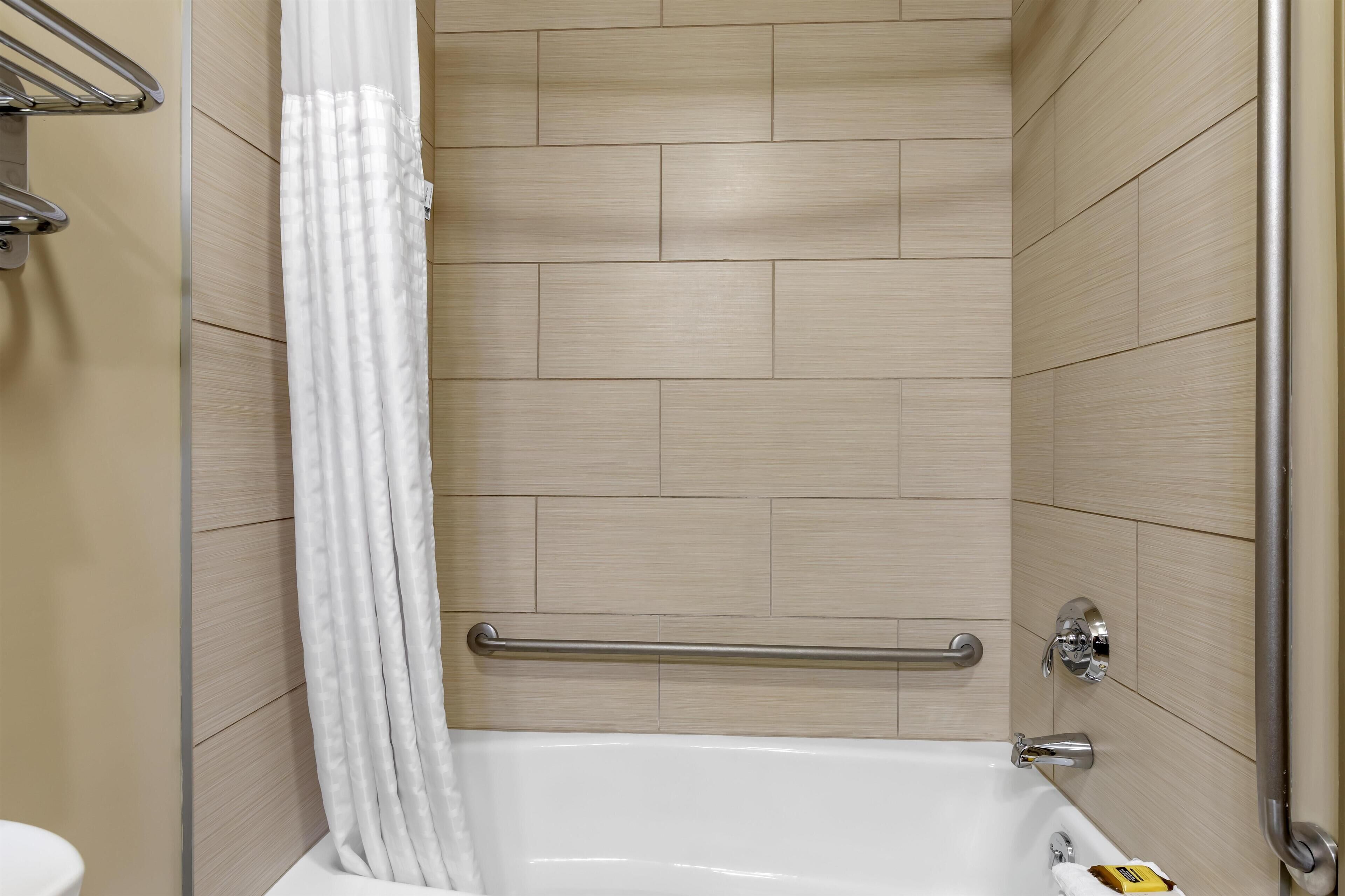 A modern bathroom with a bathtub, a shower curtain, and a handrail.