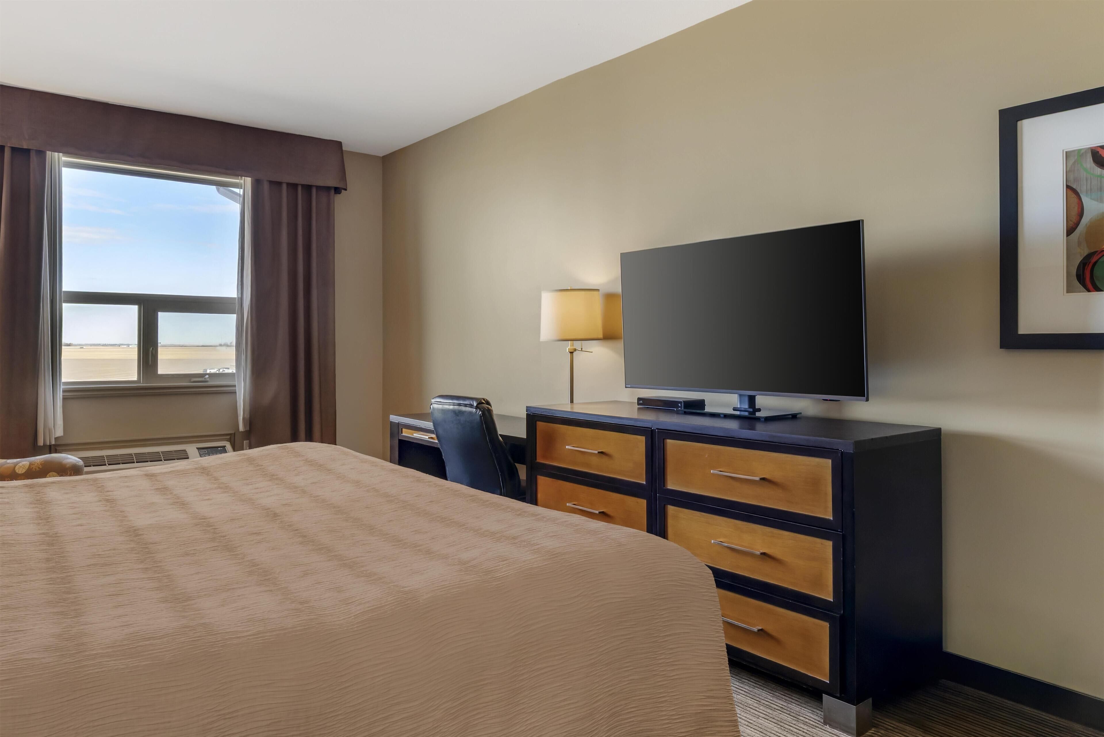 Une chambre d’hôtel avec un grand lit, un bureau avec une chaise, un téléviseur à écran plat, une lampe et un tableau encadré au mur.