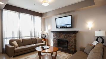 Una sala de estar con chimenea de piedra, un televisor de pantalla plana montado encima, un sofá, una mesa de centro y una lámpara.