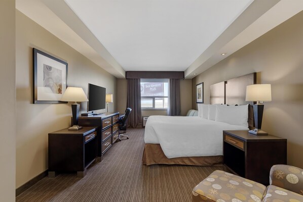 A hotel room with a bed, two bedside tables with lamps, a TV, a desk with a chair, and a large window with curtains. - Best Western Plus Moose Jaw (Moose Jaw)