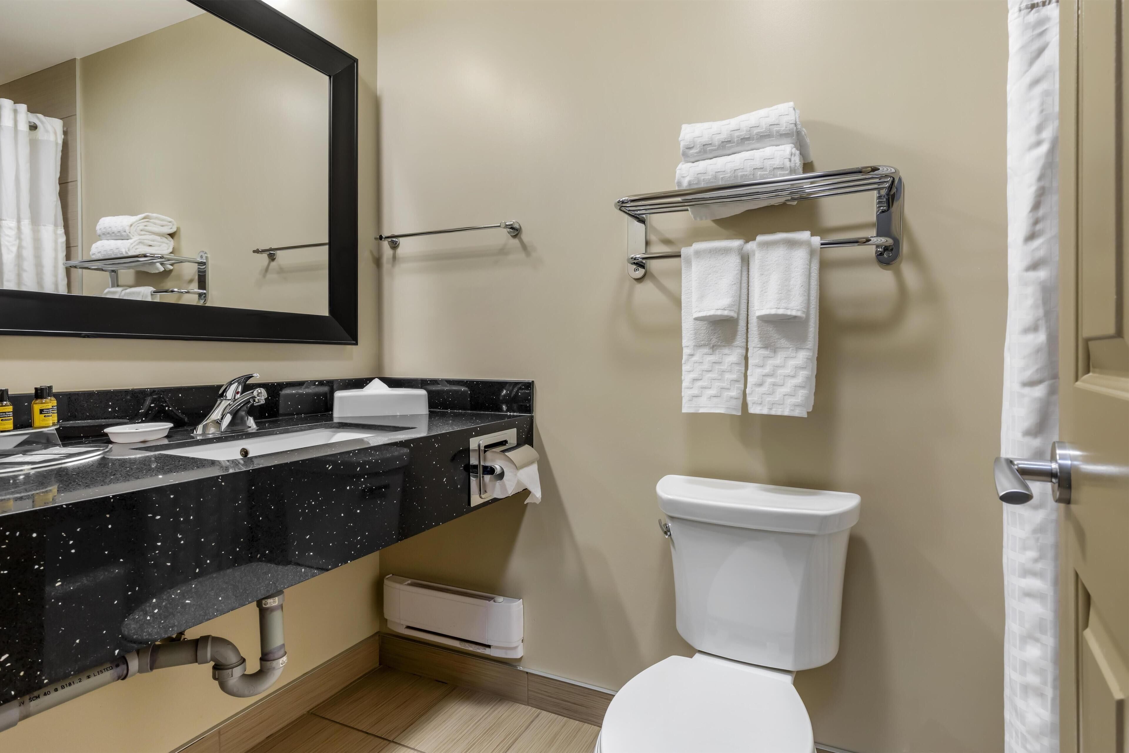 Un baño moderno con encimera negra con motas, inodoro blanco y un perchero con toallas dobladas.