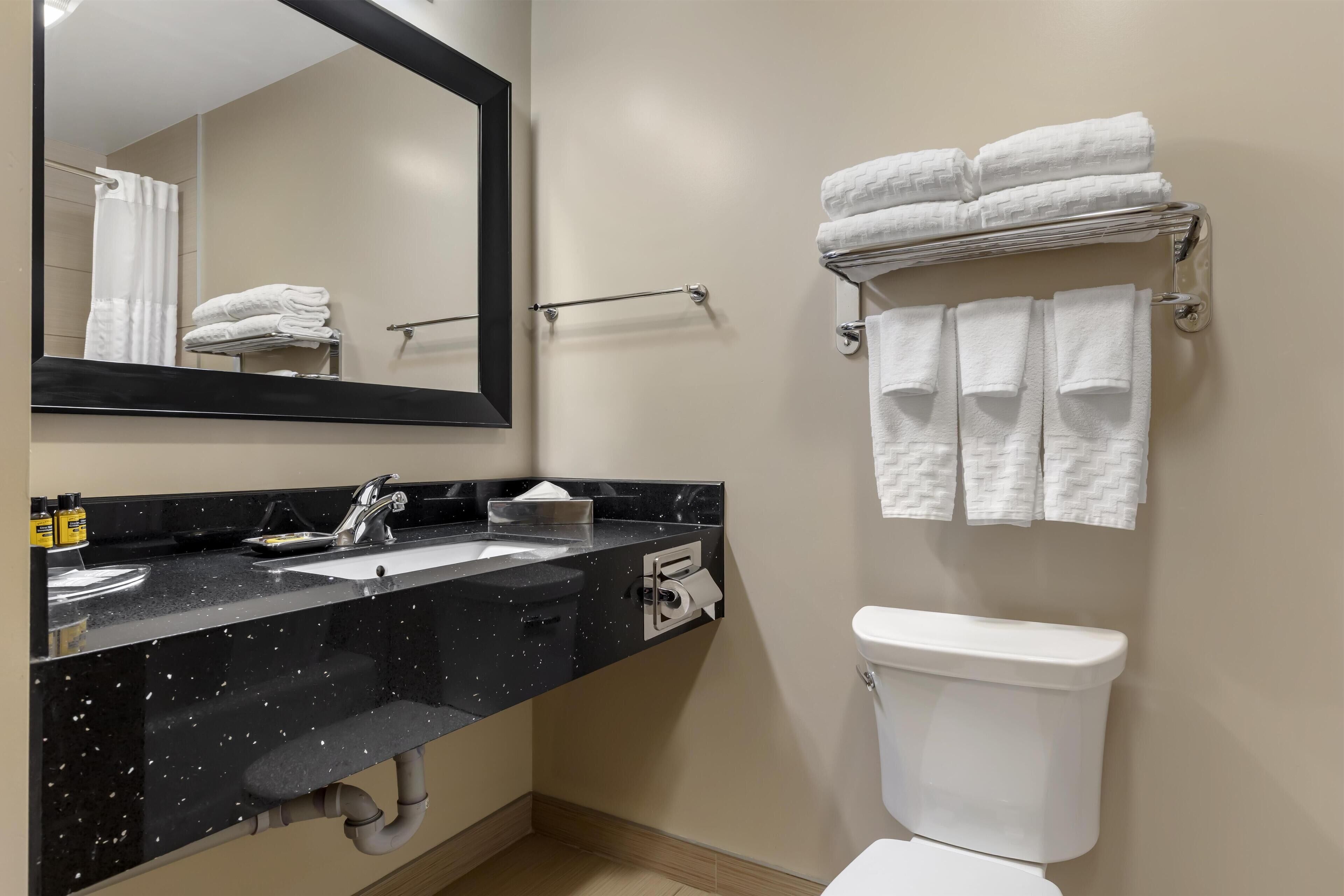 A modern bathroom with a black countertop sink, a toilet, and a towel rack with folded towels.