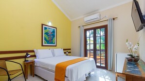 Habitación de hotel con una cama, un escritorio con computadora, una silla, un cuadro en la pared y una puerta que da a un espacio exterior.