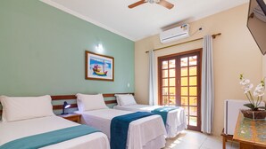 Habitación de hotel con dos camas, ventilador de techo, unidad de aire acondicionado, ventana con cortinas e imagen enmarcada en la pared.