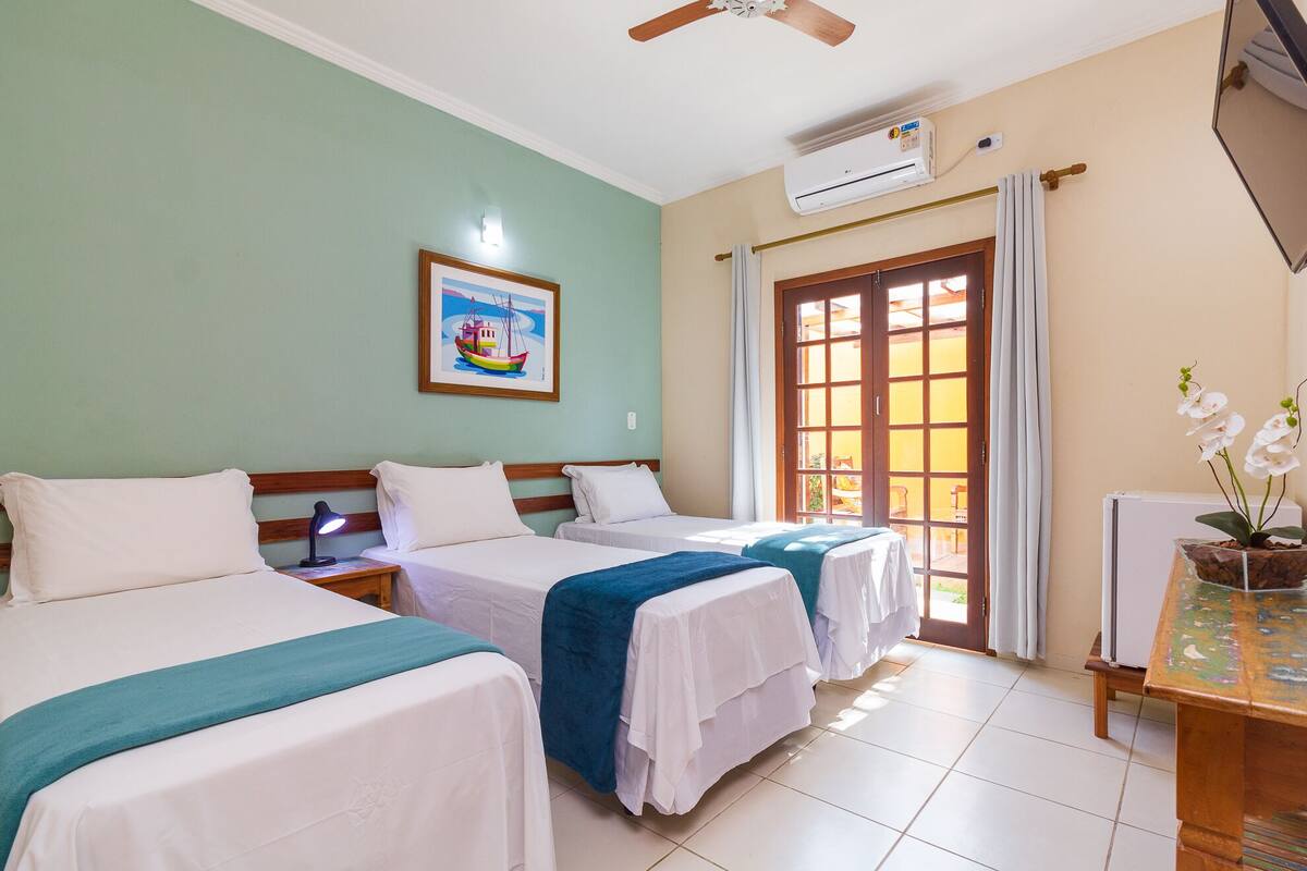 A hotel room with two beds, a ceiling fan, an air conditioning unit, a window with curtains, and a framed picture on the wall.