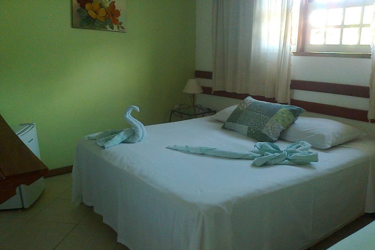 A neatly made bed with a swan-shaped towel, a quilted pillow, and a striped headboard.