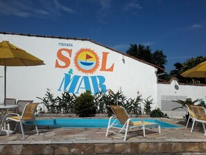 Área da piscina com espreguiçadeiras e uma placa com a inscrição 'SOL MAR', com um desenho de sol e um veleiro.