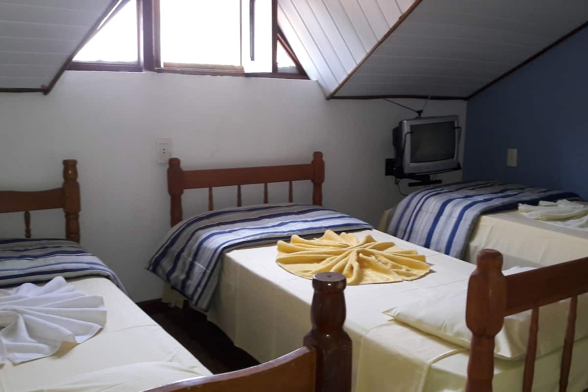 A dormitory room with three wooden beds, each with a striped bedspread and white linens. A television is mounted on the wall.