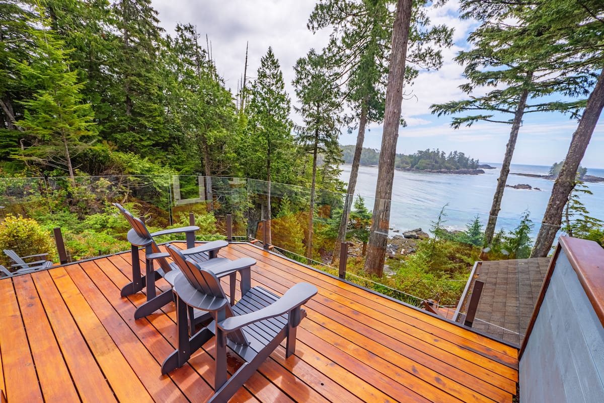 A wooden deck with Adirondack chairs overlooking a forest and a coastal view.