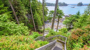 Eine Holztreppe führt zu einem Strand, gesäumt von dichtem Wald und Felsformationen.