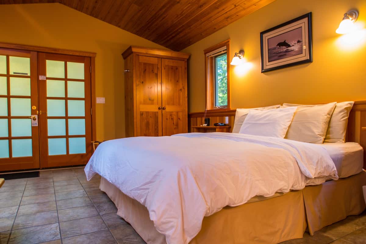 A bedroom with a large bed, wooden wardrobe, and a small table with a lamp.