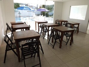 A dining area with wooden tables and chairs, large windows, and a view of an outdoor swimming pool area. - Pousada Vila do Galo (Ipojuca)