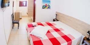 Ein Hotelzimmer mit einem Bett, einem Sessel, einem Schreibtisch, einem Fernseher und einem Bild an der Wand.