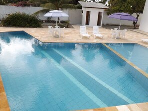 A swimming pool with clear blue water, surrounded by white lounge chairs and umbrellas. - Pousada Vila do Galo (Ipojuca)
