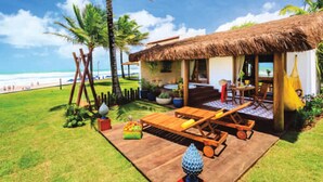 A beach house with a thatched roof, wooden deck, and outdoor seating area. - Village Porto de Galinhas (Ipojuca)