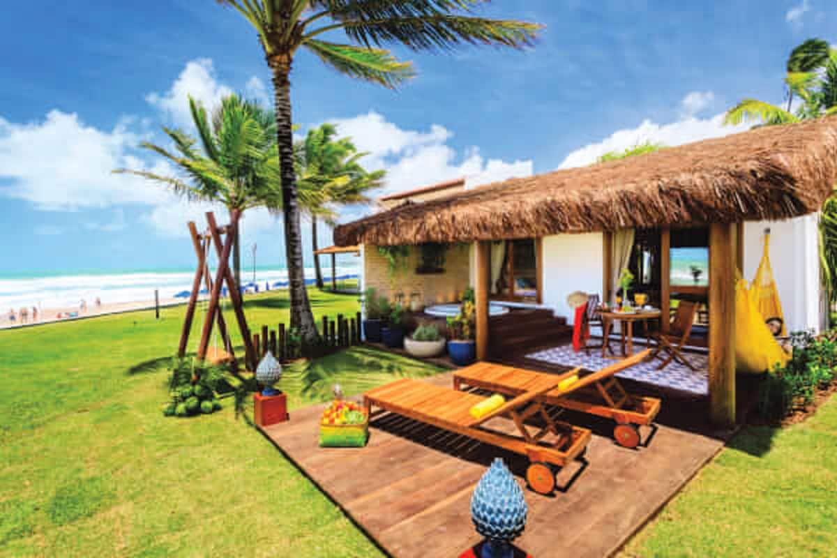 Ein Strandhaus mit Strohdach, Holzterrasse und Sitzbereich im Freien.