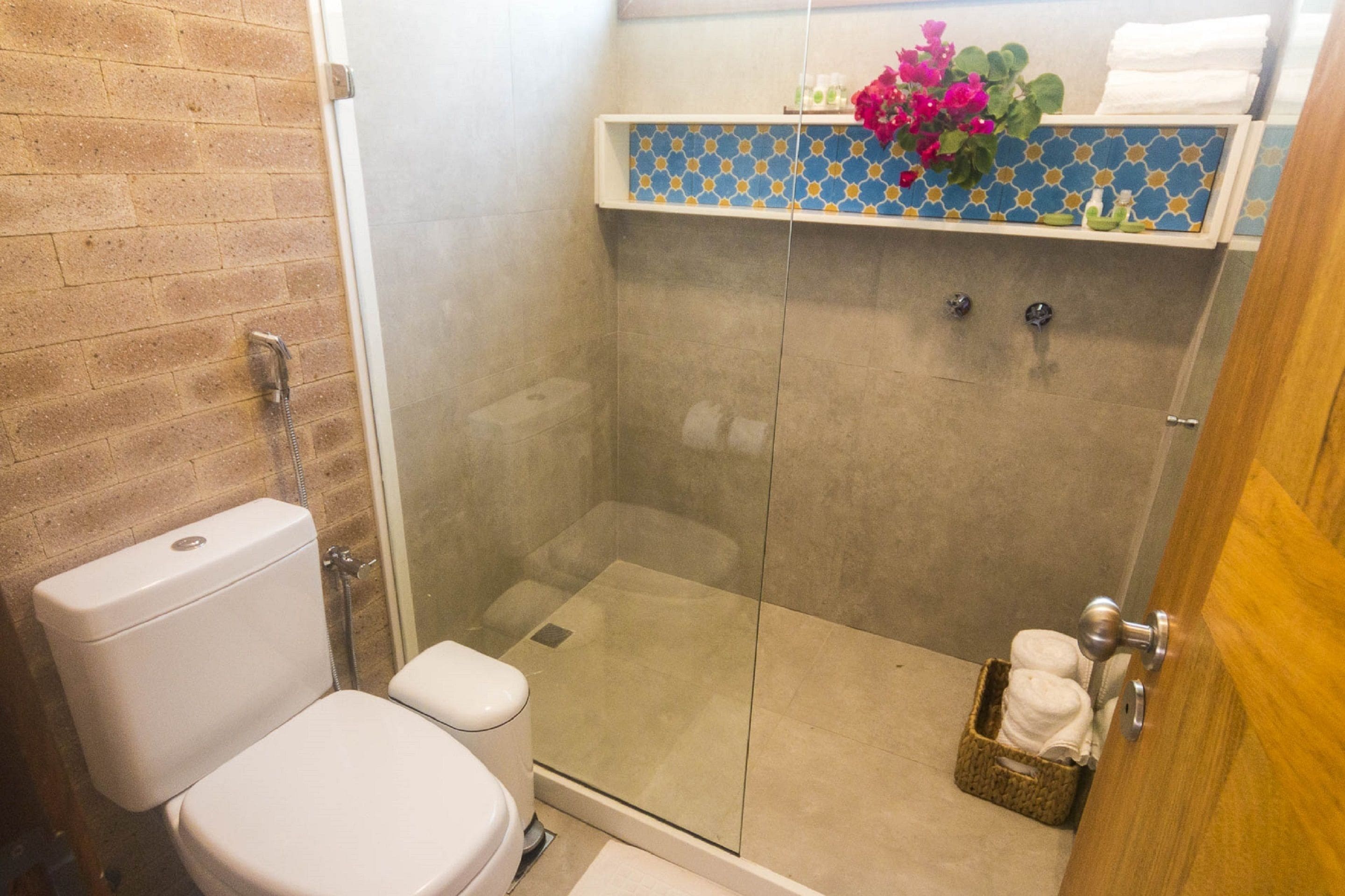 A bathroom with a glass-enclosed shower, a toilet, and a shelf with toiletries.