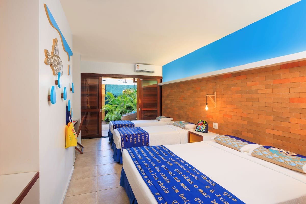 Ein Hotelzimmer mit zwei Betten, einer Ziegelwand, einer blauen Decke und Blick auf Grünfläche.
