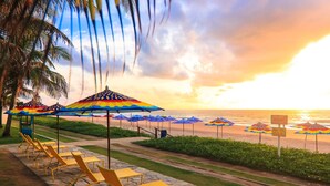 A beachside lounge with yellow chairs and colorful umbrellas, a stone pathway, and a view of the ocean at sunset. - Village Porto de Galinhas (Ipojuca)