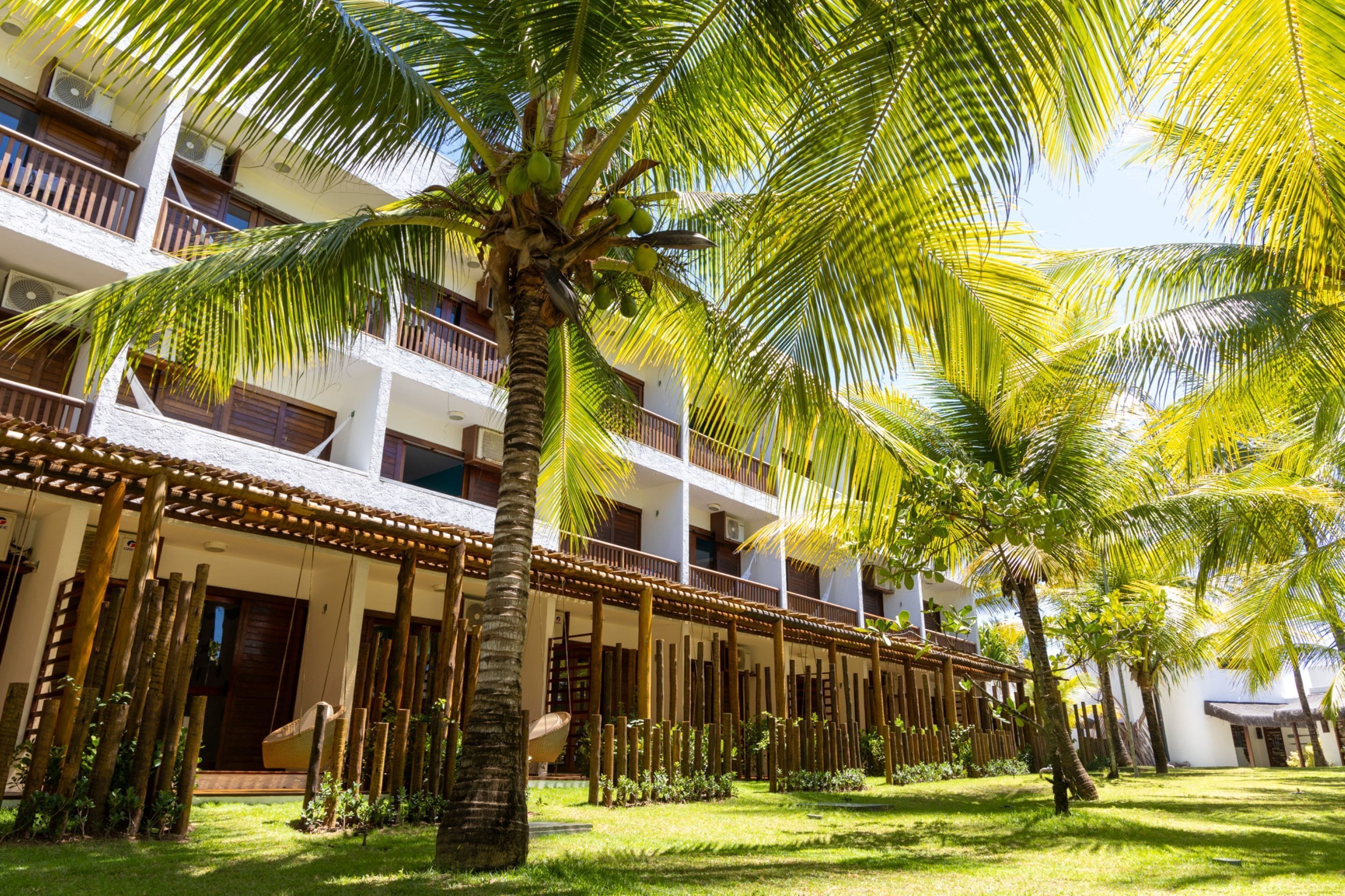 A hotel with multiple balconies, palm trees, and a covered outdoor seating area.