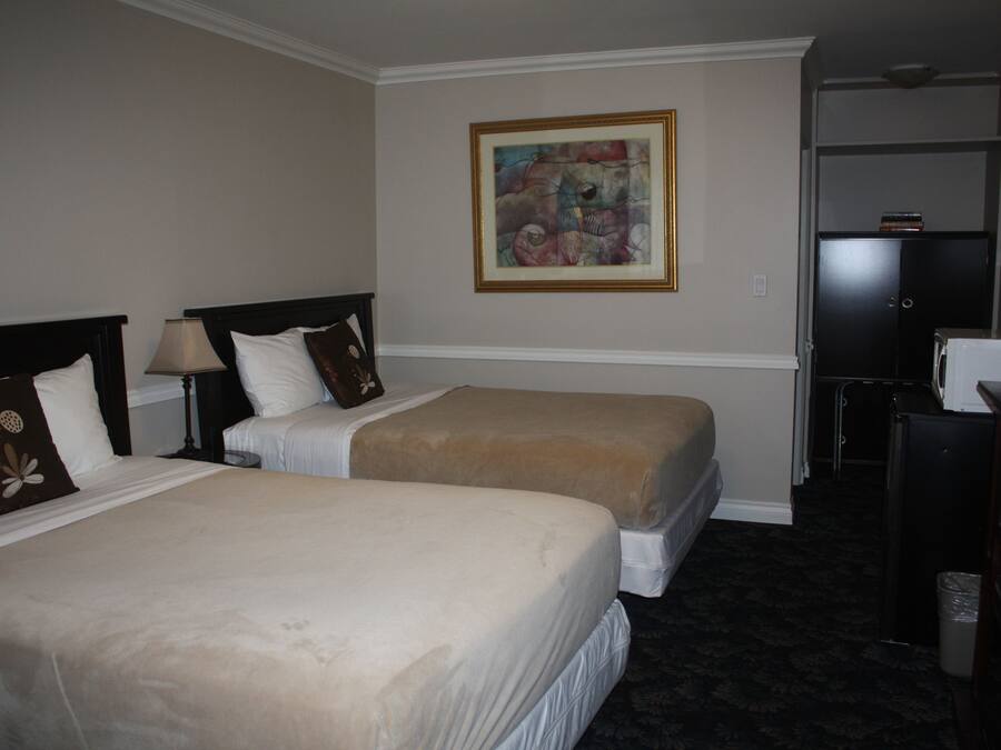 A hotel room with two beds, a painting on the wall, a desk, and a trash bin.
