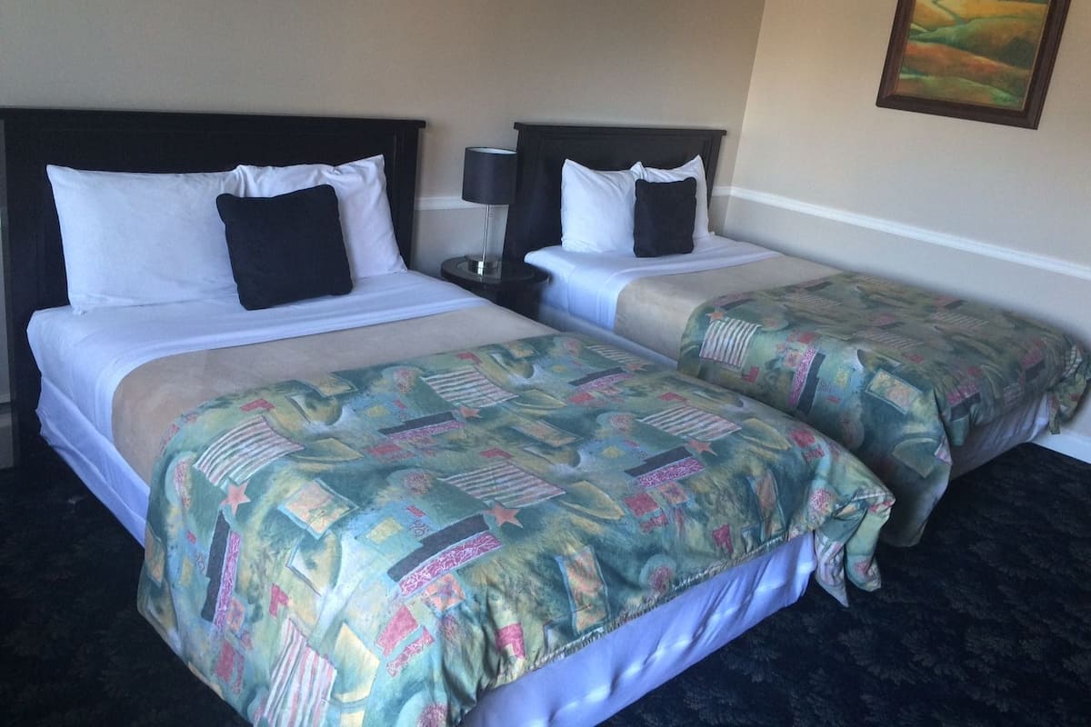 Camera d'albergo con due letti, ognuno dotato di testiera, biancheria da letto bianca e copripiumino decorato.