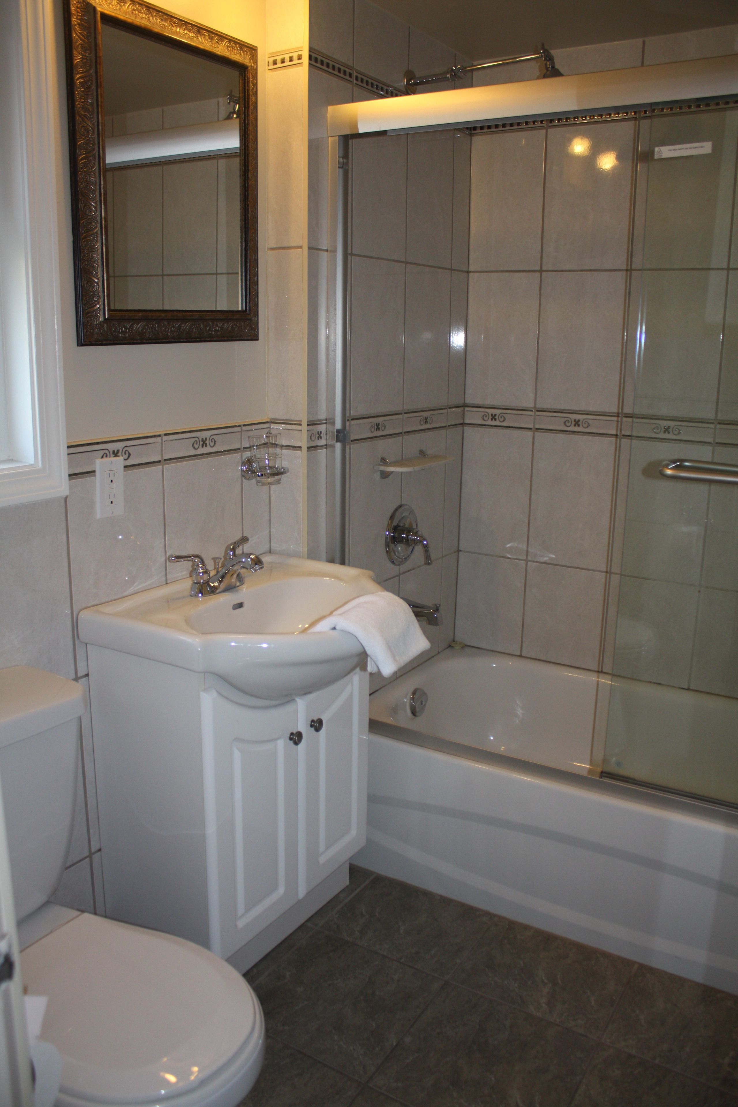 Un baño con lavamanos blanco, espejo, inodoro y ducha con mampara de vidrio.