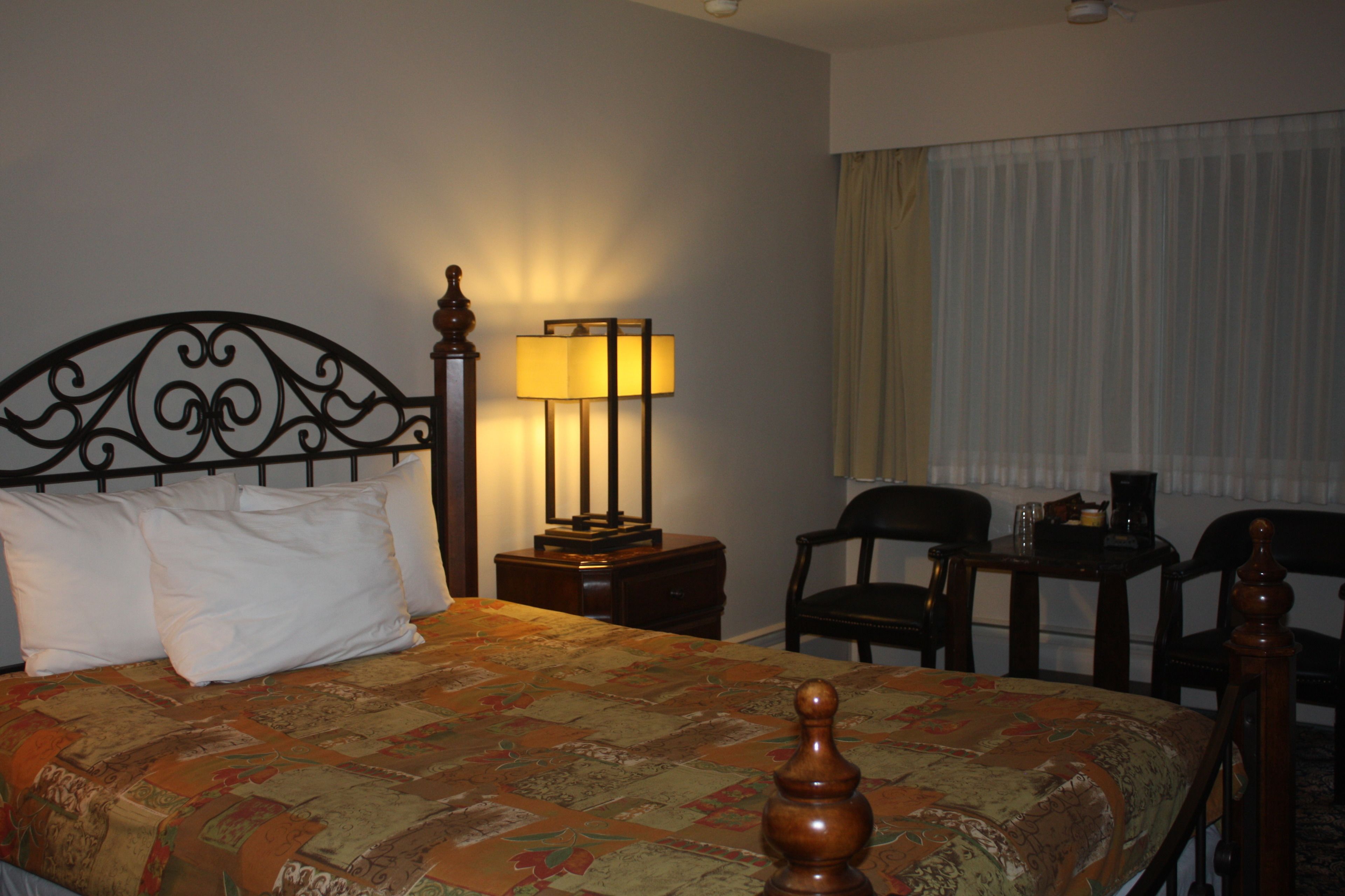 A hotel room with a bed, a desk, a chair, a lamp, and a window with curtains.