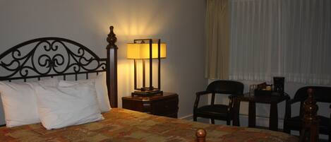 A hotel room with a bed, a desk, a chair, a lamp, and a window with curtains.