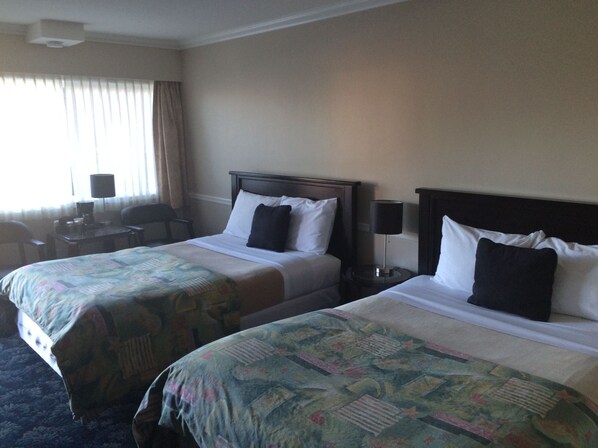 A hotel room with two beds, a desk, a chair, and a lamp.