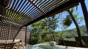 Een bubbelbadgedeelte met een houten pergola, een zithoek en uitzicht op een bergachtig landschap.
