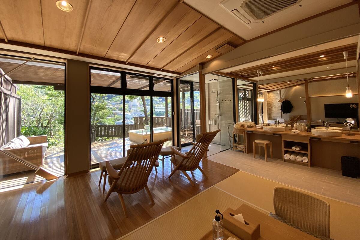 Een modern interieur met houten vloeren, een eetgedeelte met stoelen, een keuken met een bar en grote ramen met uitzicht op de omgeving.