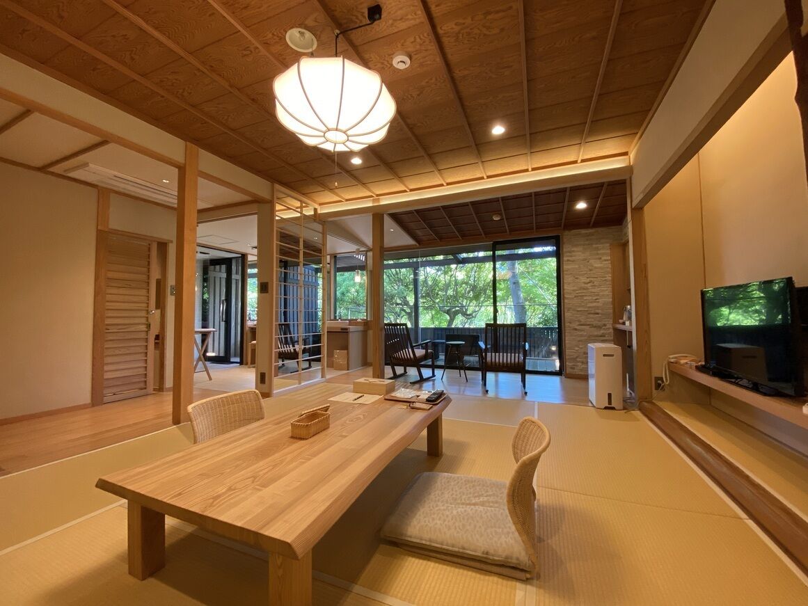 Una habitación tradicional japonesa con suelo de tatami, una mesa de comedor de madera y un televisor en la pared.