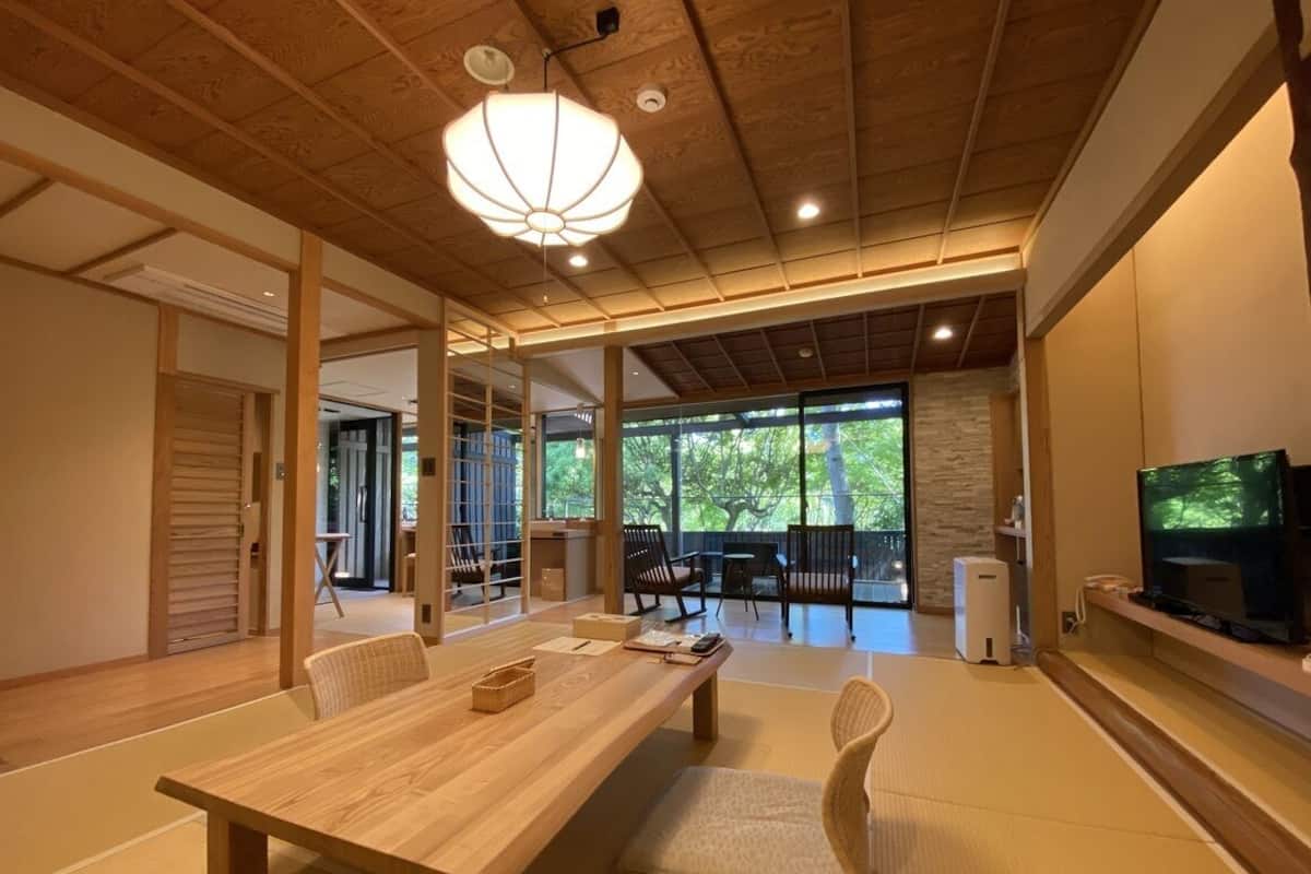 Una habitación tradicional japonesa con suelo de tatami, una mesa de comedor de madera y un televisor en la pared.