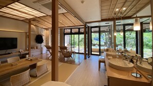 Een moderne hotelkamer met een zithoek, een groot raam en een badkamer met wastafel en spiegel.