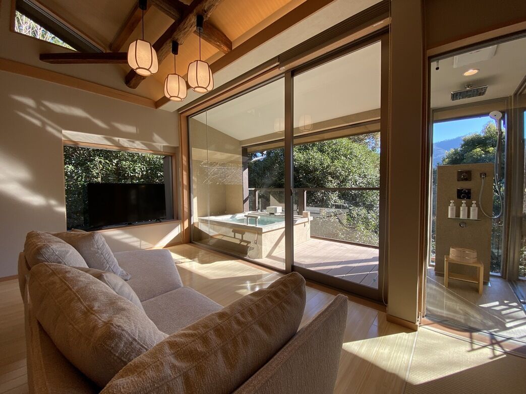 A modern living room with a large sofa, a glass-enclosed balcony, and a TV.