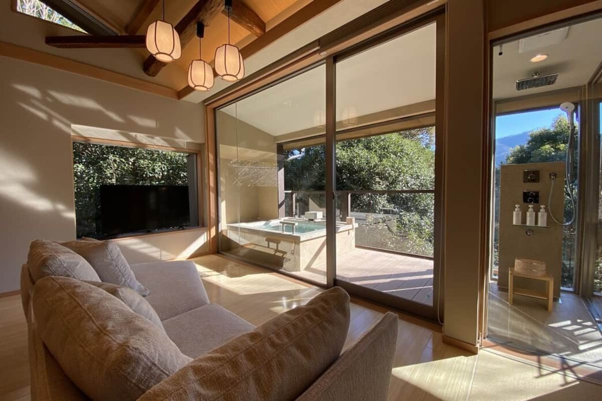 A modern living room with a large sofa, a glass-enclosed balcony, and a TV.