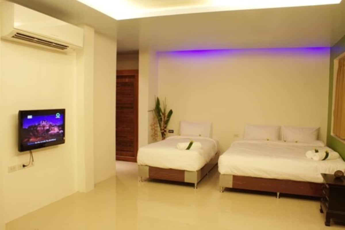 Habitación de hotel con dos camas, un televisor de pantalla plana montado en la pared y una planta en maceta.
