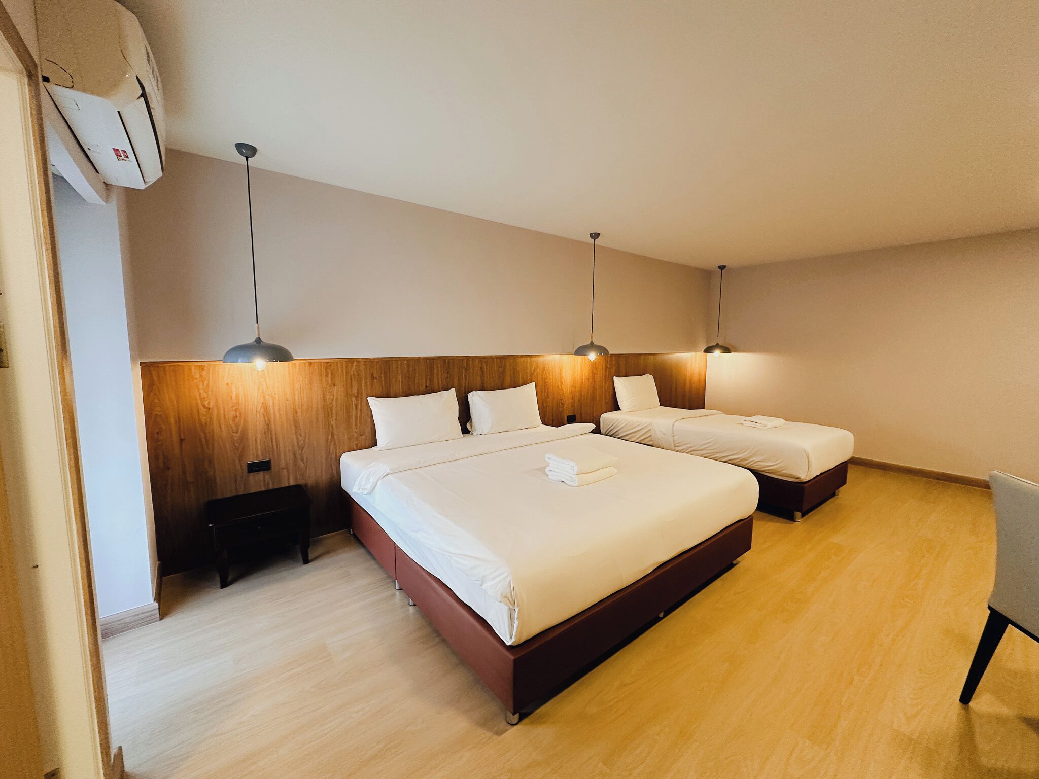 A hotel room with two beds, wooden headboard, bedside lamps, and a wooden floor.