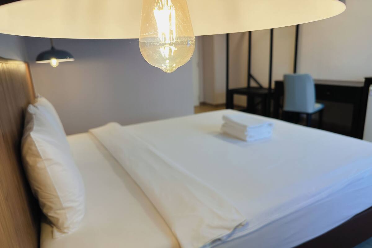 A neatly made bed with white linens and a folded towel on the headboard.