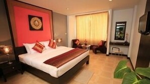 A hotel room with a large bed, a desk, a chair, a television, and a plant. - CS Park (Koh Samui)