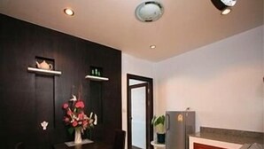 A compact kitchen with a dining area, featuring a dark wooden wall, a small refrigerator, and a table with chairs. - CS Park (Koh Samui)