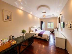 A hotel room with a bed, a desk, a small kitchenette, a window, and a ceiling light fixture.